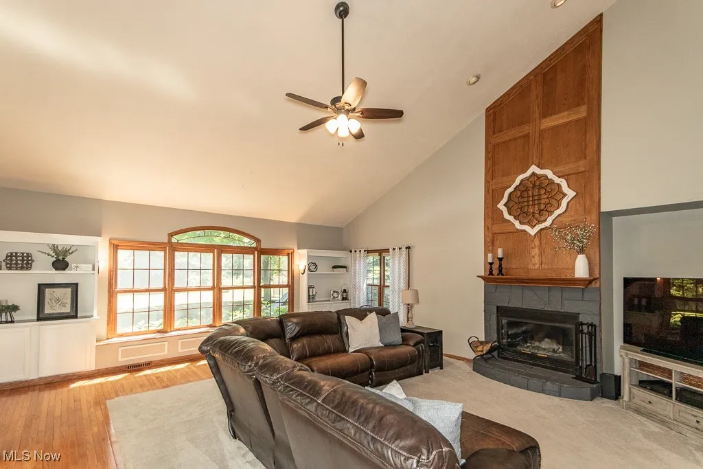 Living area featuring high vaulted ceiling, a ceiling fan, a tile fireplace, and built in shelves
