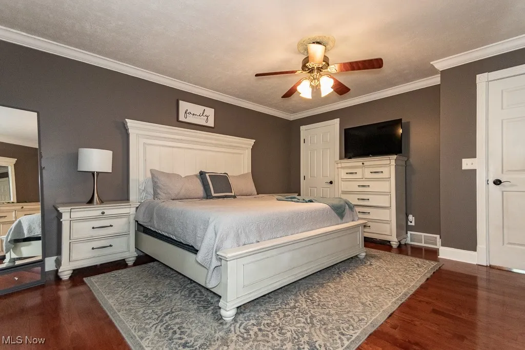 Bedroom featuring dark wood-style flooring, ornamental molding, and a ceiling fan