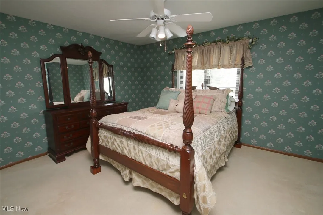 Carpeted bedroom featuring ceiling fan and wallpapered walls