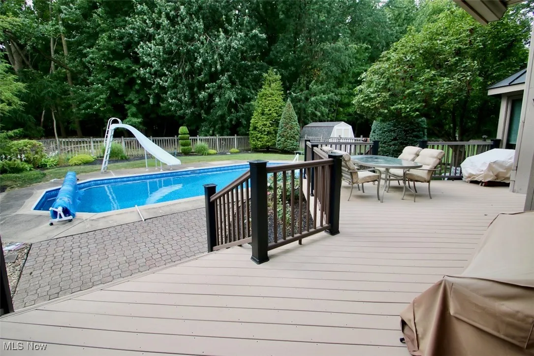 View of swimming pool with outdoor dining area, a water slide, a deck, and a fenced backyard