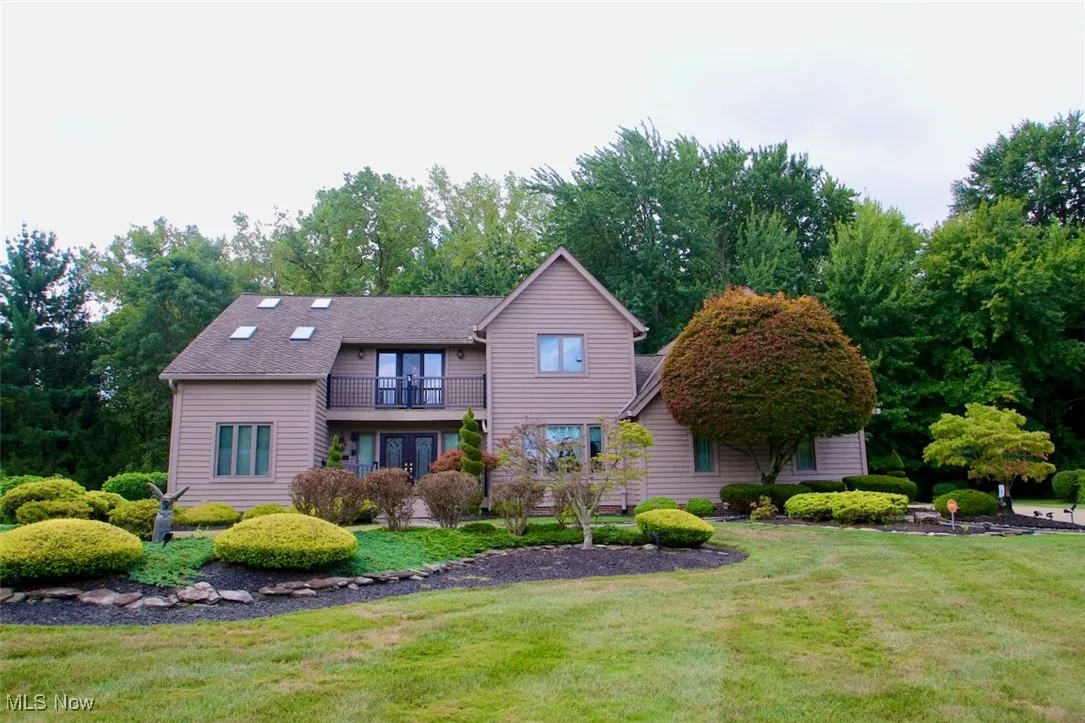 View of front of house featuring a balcony, a front yard, and view of scattered trees