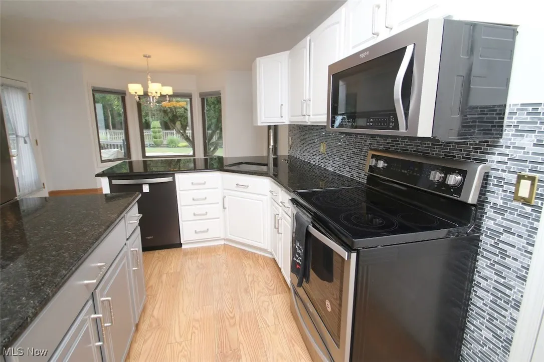 Kitchen featuring appliances with stainless steel finishes, light wood-style flooring, dark granite countertops, and decorative light fixtures