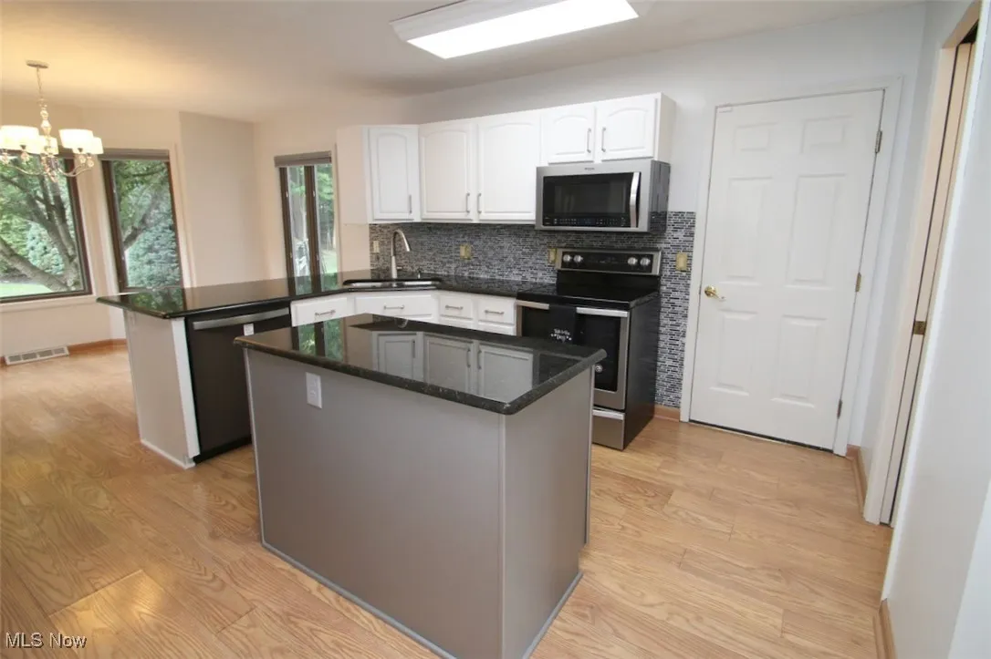 Kitchen with stainless steel appliances, a peninsula, tasteful backsplash, a center island, and white cabinetry