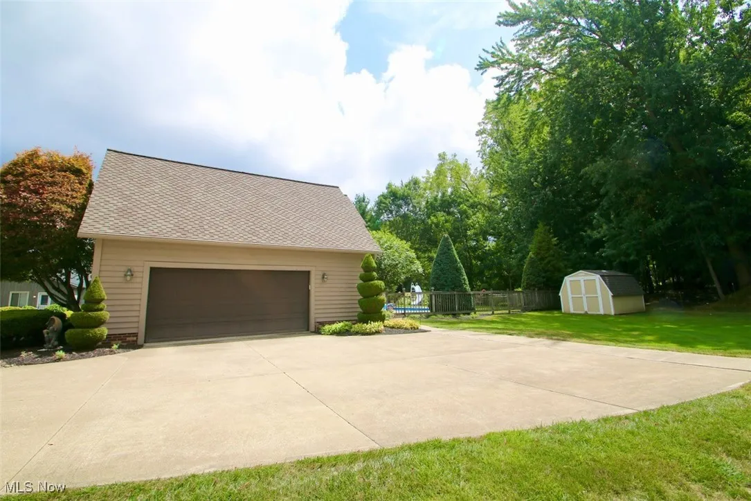 View of home's exterior with a shed, a garage, concrete driveway, and roof with shingles