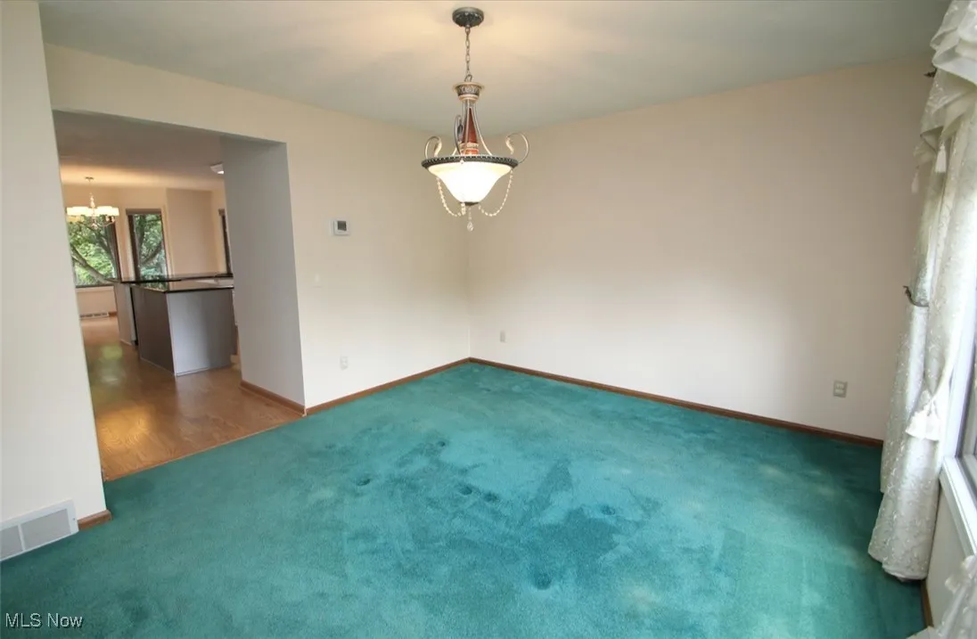 Carpeted empty room with a chandelier and baseboards