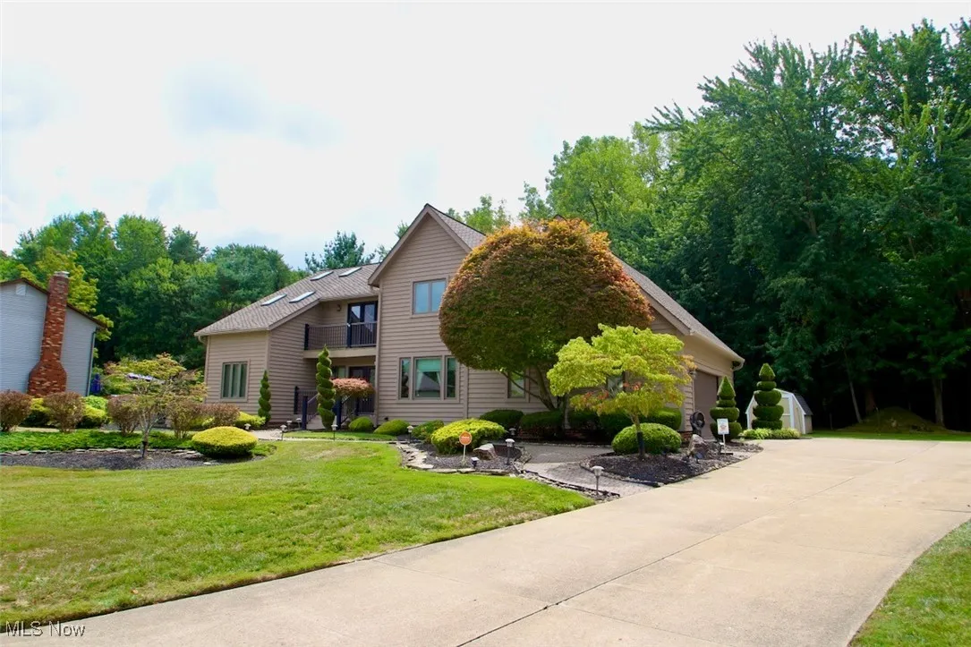 View of front of home featuring a front yard, driveway, a garage, view of scattered trees, and a balcony
