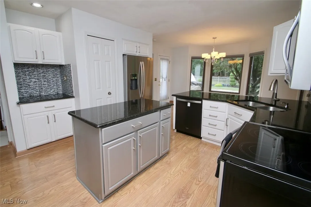 Kitchen with gray cabinets, black appliances, decorative backsplash, dark granite counters, and a peninsula