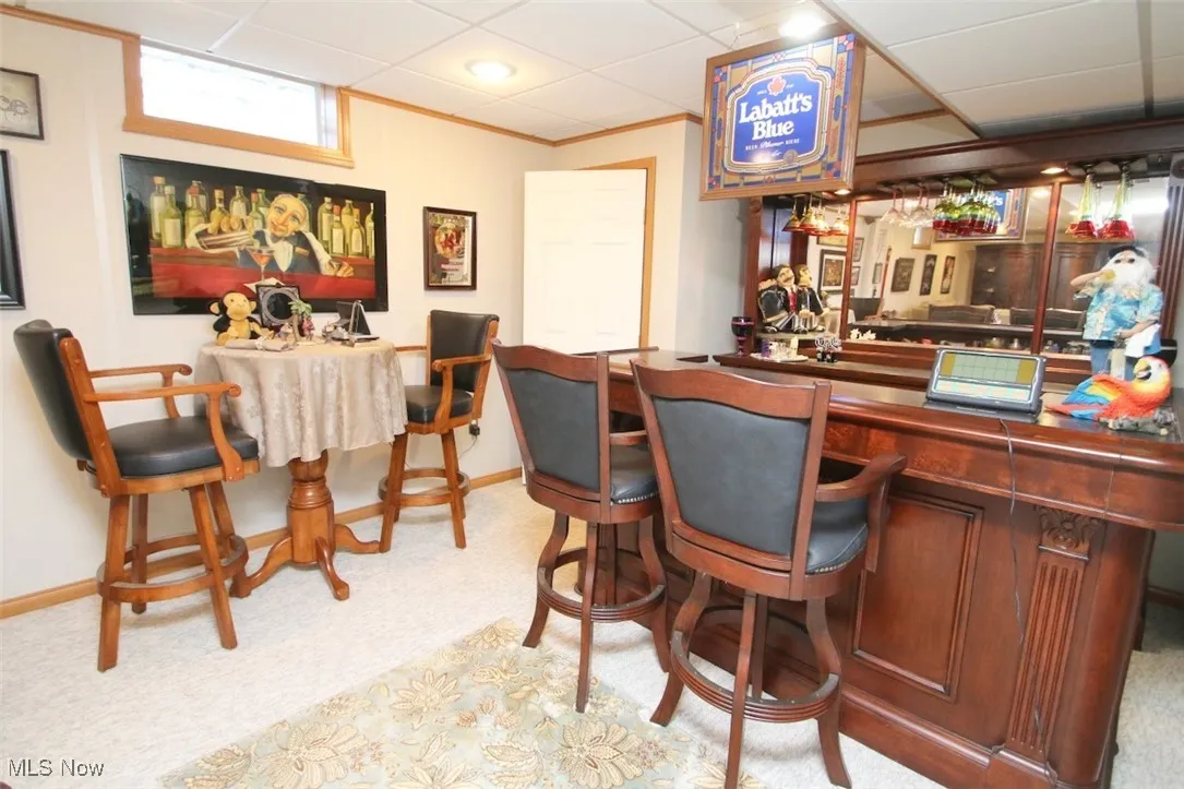 Indoor dry bar featuring light carpet, dark countertops, crown molding, and a paneled ceiling