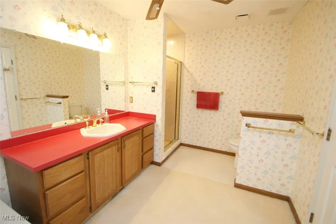 Full bathroom with vanity, a stall shower, wallpapered walls, and a ceiling fan
