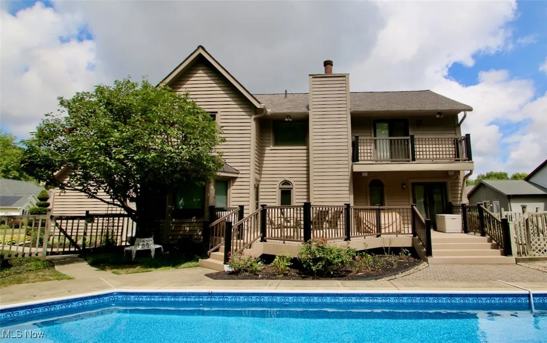 Back of house with an outdoor pool, a chimney, a balcony, and stairs