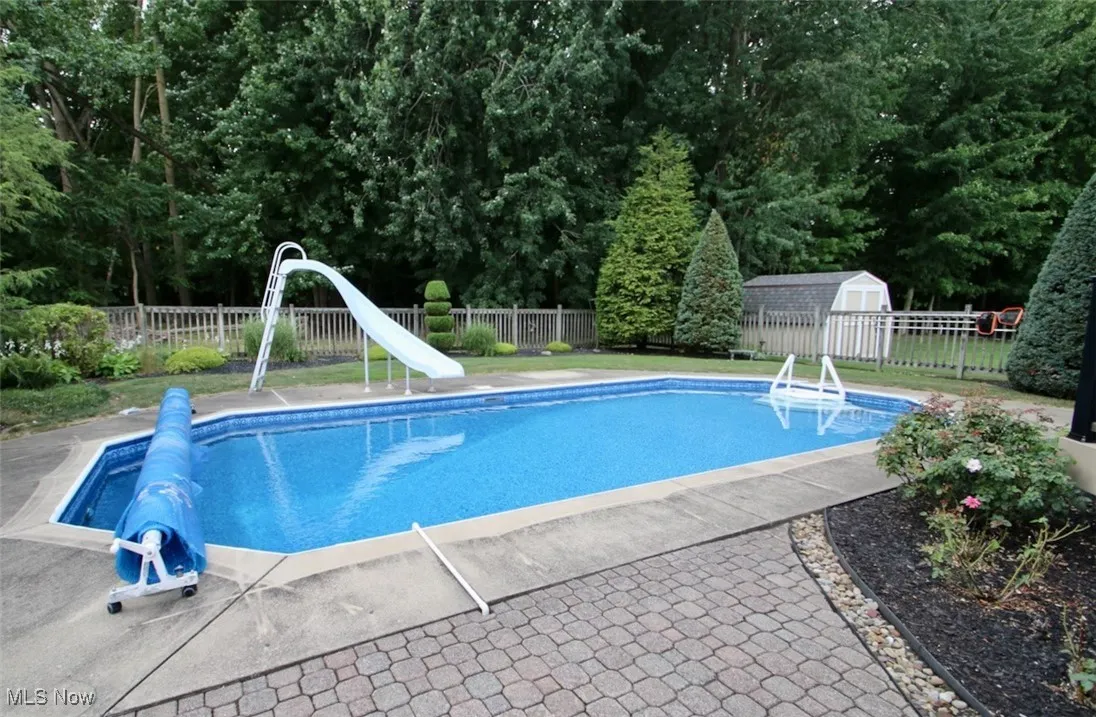 View of pool featuring a water slide, a fenced backyard, a storage shed, and a patio area