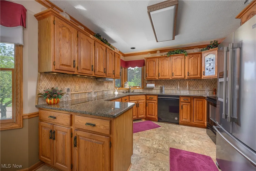 Kitchen featuring brown cabinetry, backsplash, black appliances, dark stone counters, and a textured ceiling