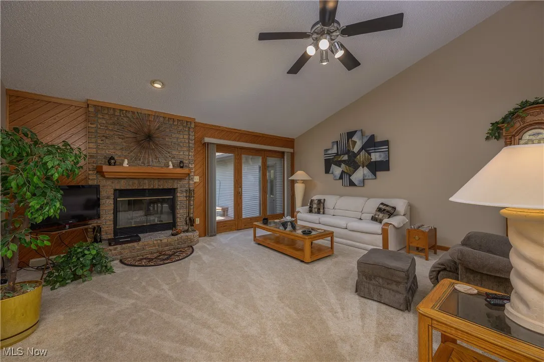 Carpeted living room with a textured ceiling, a brick fireplace, wood walls, lofted ceiling, and a ceiling fan