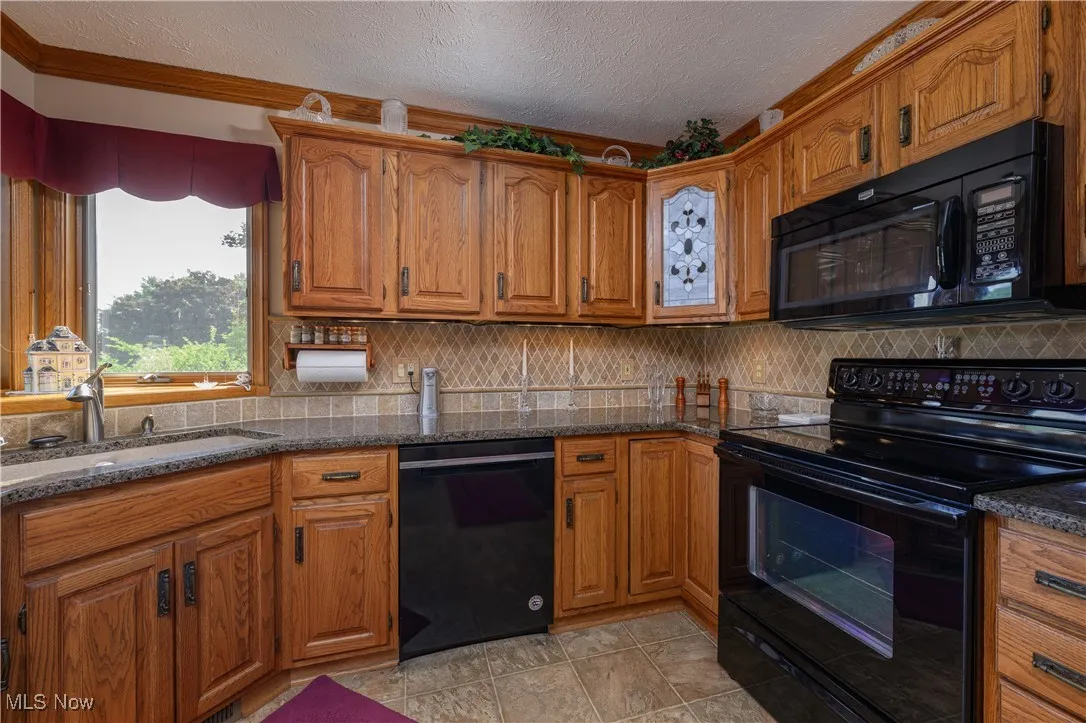 Kitchen with brown cabinetry, black appliances, a textured ceiling, decorative backsplash, and dark stone countertops