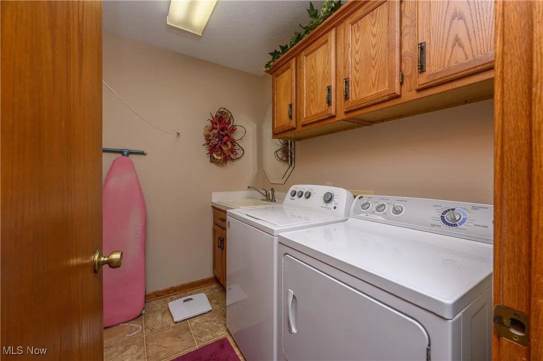 Laundry room featuring washing machine and clothes dryer, cabinet space, light tile patterned floors, and a textured ceiling