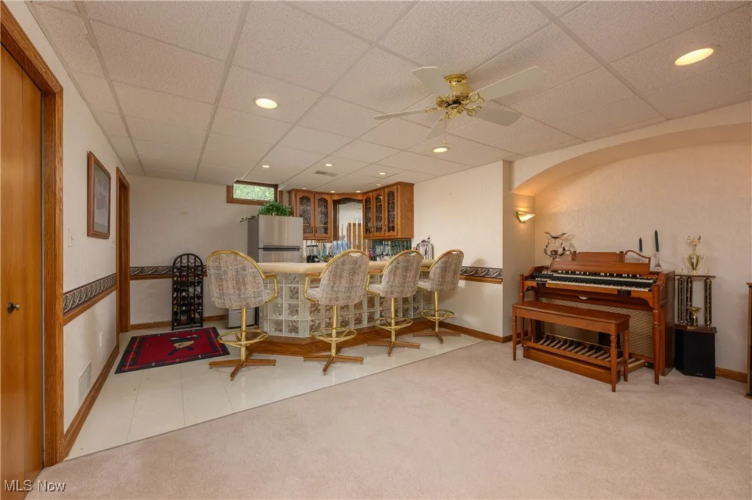 Dining space featuring a drop ceiling, light carpet, recessed lighting, bar area, and a ceiling fan