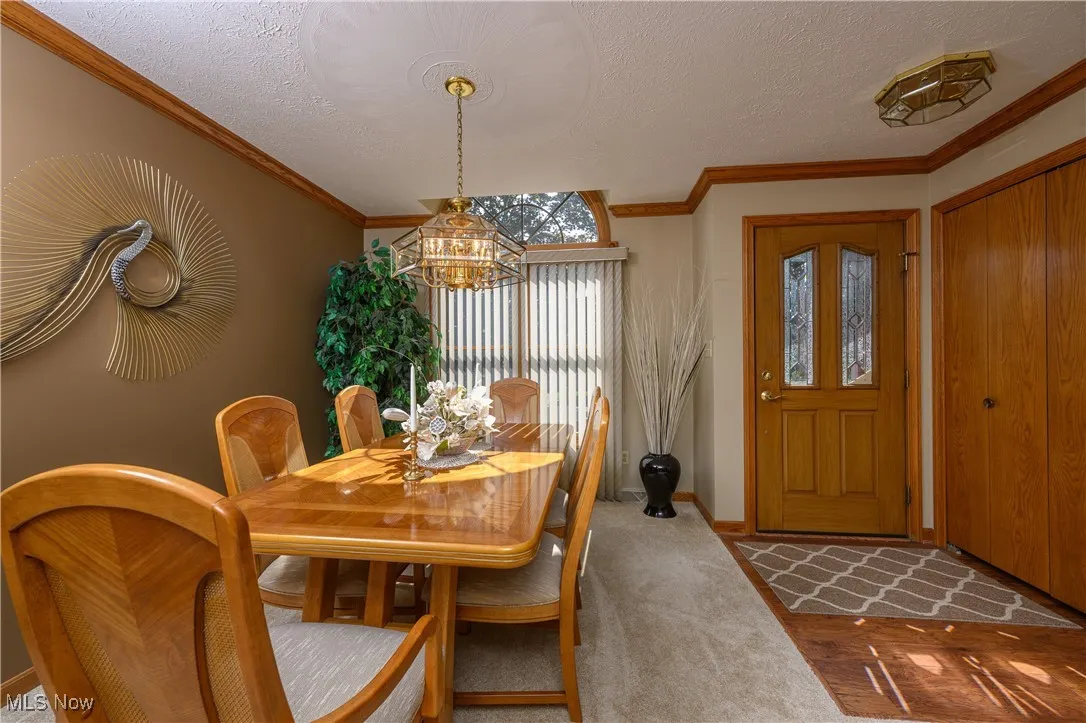 Dining space featuring a textured ceiling, crown molding, carpet flooring, and a chandelier