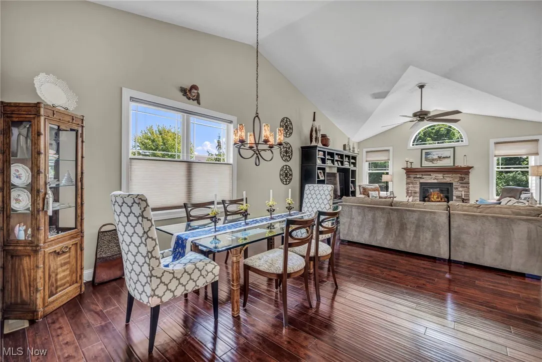 Dining area with dark wood-style floors, a fireplace, a chandelier, ceiling fan, and high vaulted ceiling