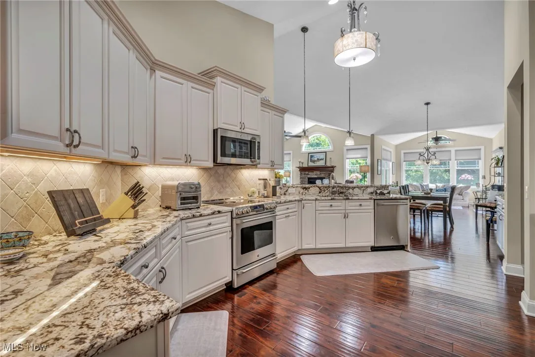 Kitchen with appliances with stainless steel finishes, a peninsula, decorative light fixtures, light stone counters, and high vaulted ceiling
