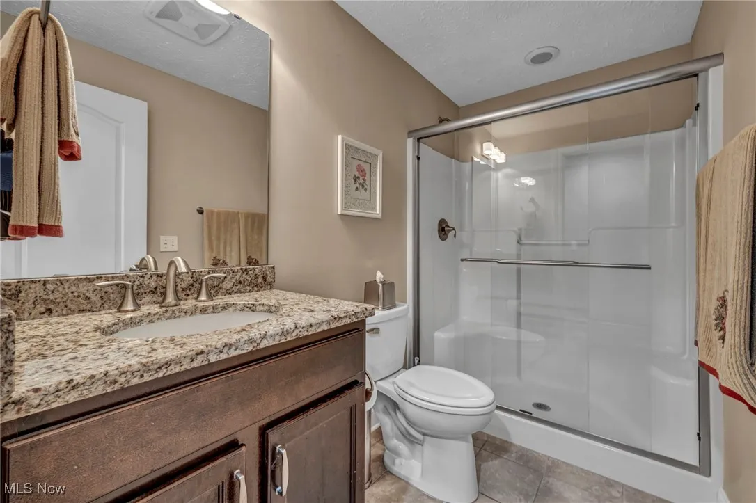 Full bath featuring vanity, a textured ceiling, a shower stall, and light tile patterned floors