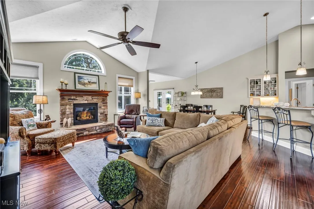 Living room with high vaulted ceiling, dark wood-style floors, a stone fireplace, and ceiling fan