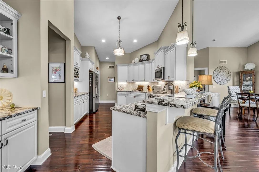 Kitchen with light granite countertops, a breakfast bar, dark wood-type flooring, tasteful backsplash, and recessed lighting