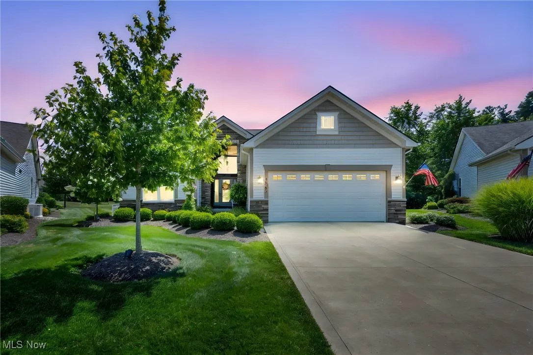 Craftsman-style house with stone siding, driveway, a garage, and a lawn