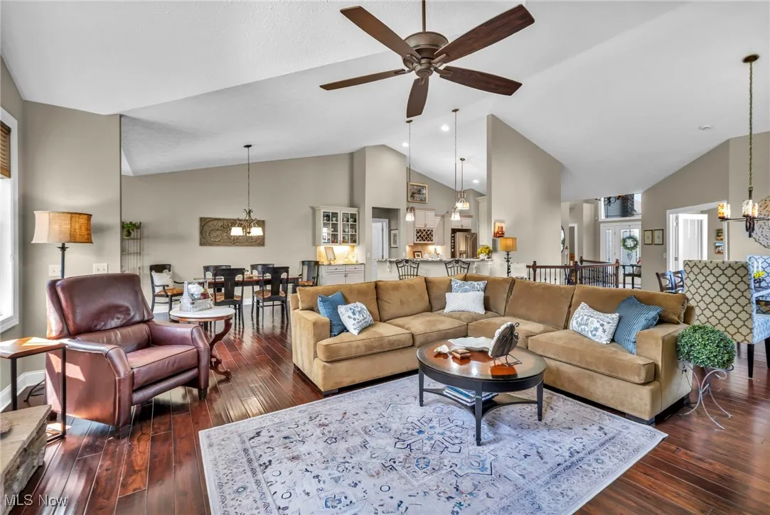 Living area featuring a chandelier, high vaulted ceiling, dark wood-style floors, and ceiling fan