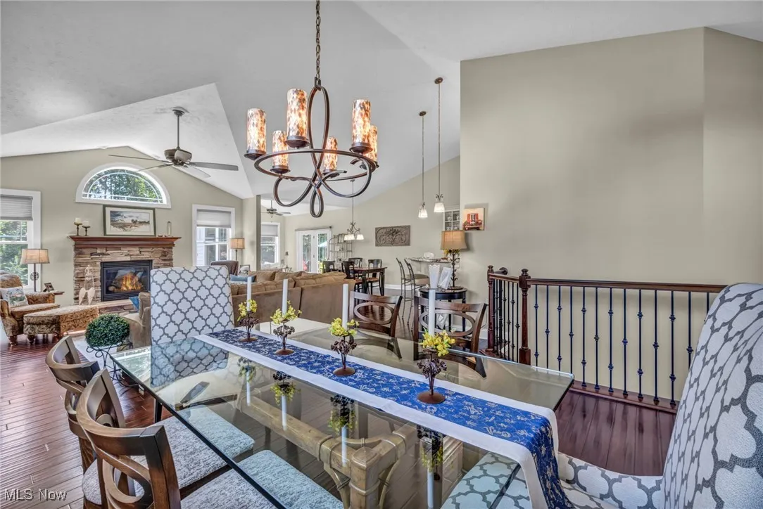Dining area featuring a chandelier, wood-type flooring, high vaulted ceiling, a fireplace, and a ceiling fan