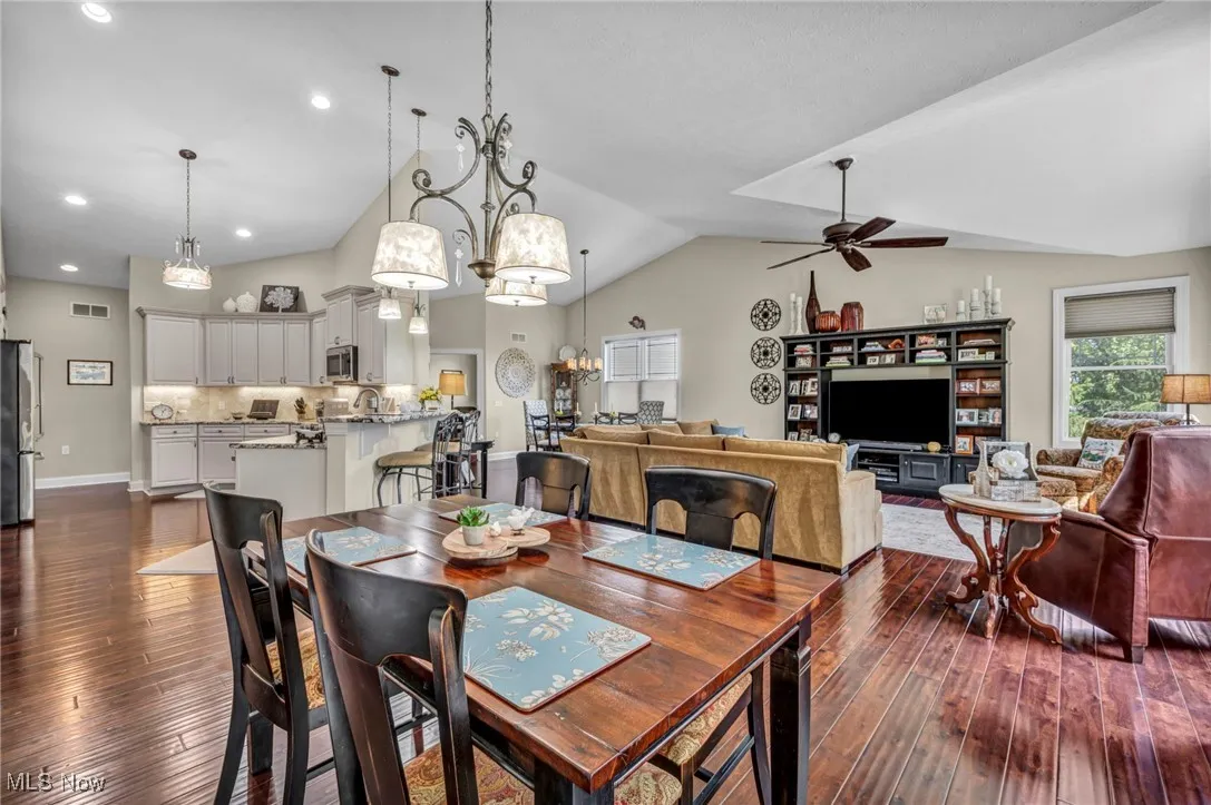 Dining space with a chandelier, lofted ceiling, a ceiling fan, and dark wood-style floors