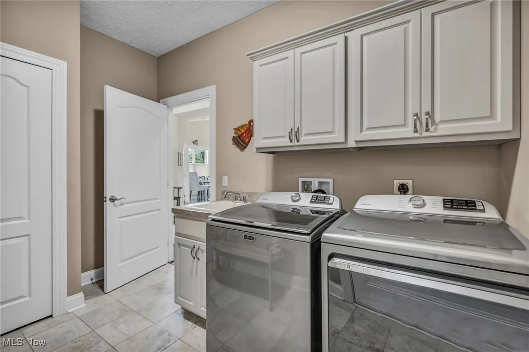 Laundry room with cabinet space, washing machine and clothes dryer, a textured ceiling, and light tile patterned floors