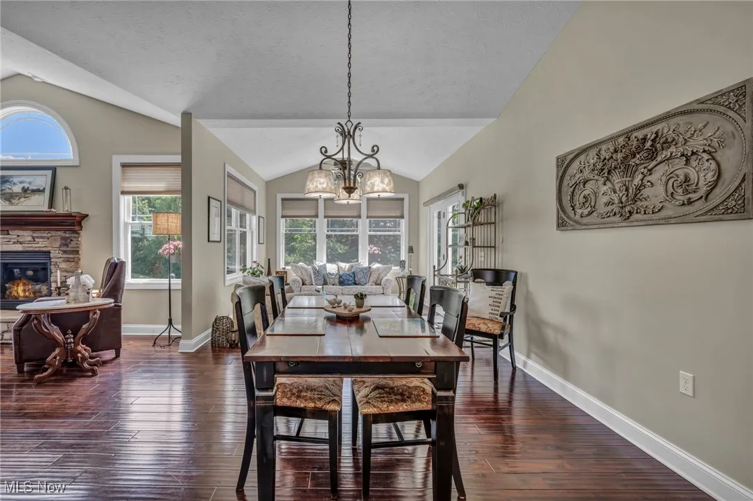 Dining space featuring vaulted ceiling, a stone fireplace, a chandelier, dark wood-style floors, and a textured ceiling
