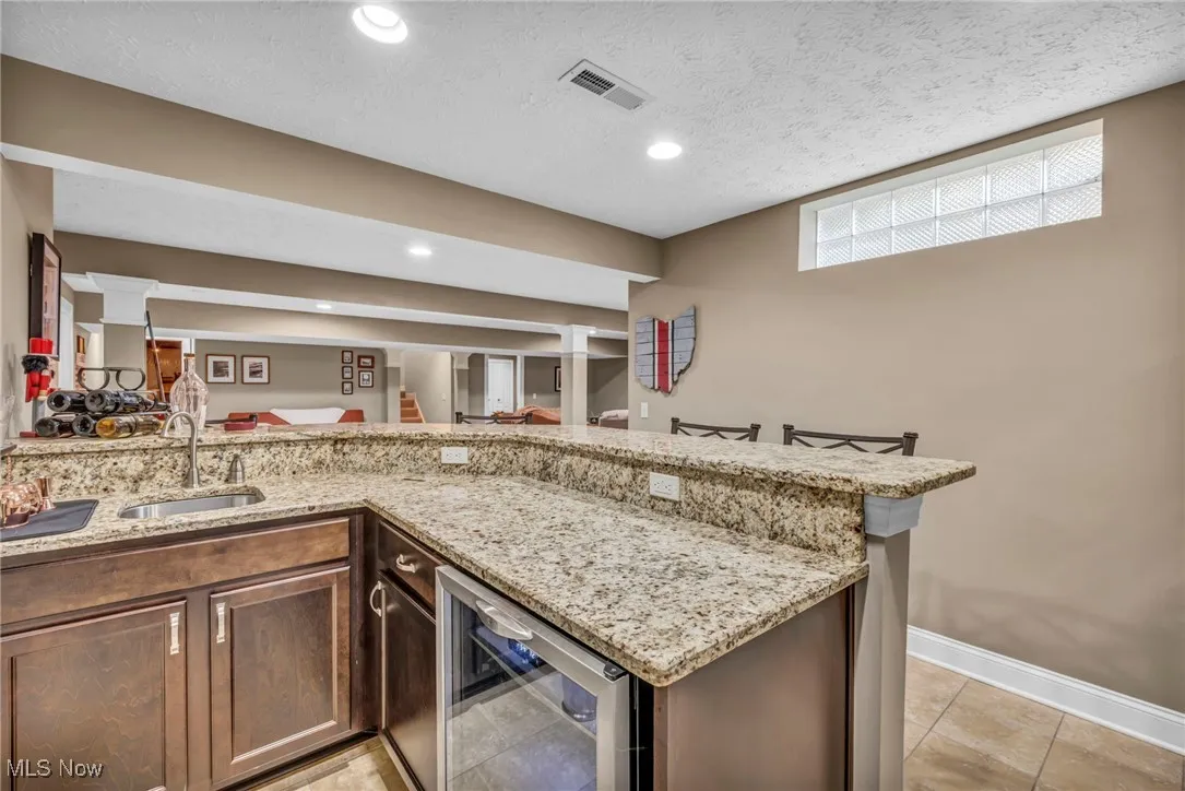 Kitchen featuring light granite countertops, a textured ceiling, wine cooler, recessed lighting, and light tile patterned floors