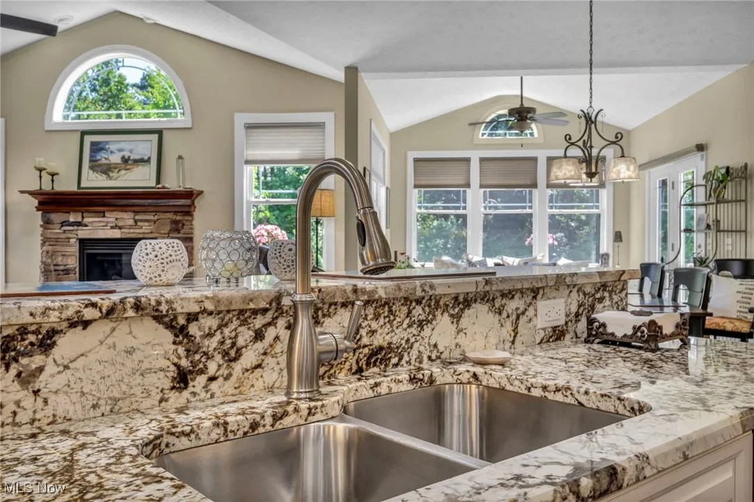 Kitchen featuring light granite countertops, vaulted ceiling, hanging light fixtures, a fireplace, and plenty of natural light