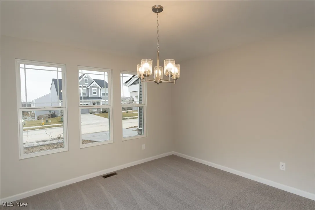 Empty room featuring light colored carpet and a chandelier