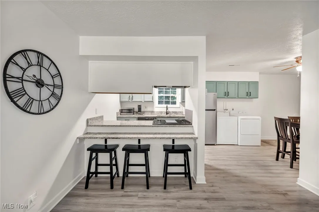 Kitchen featuring a breakfast bar area, light wood-style floors, freestanding refrigerator, separate washer and dryer, and a textured ceiling
