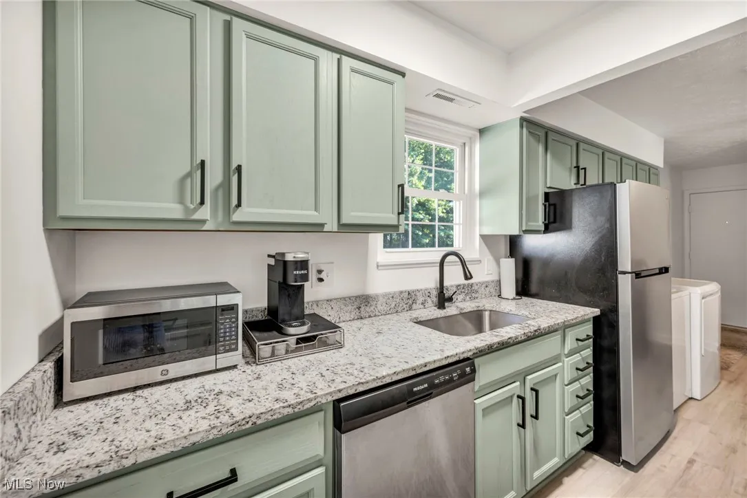 Kitchen with green cabinetry, light stone countertops, appliances with stainless steel finishes, light wood-type flooring, and washer / dryer
