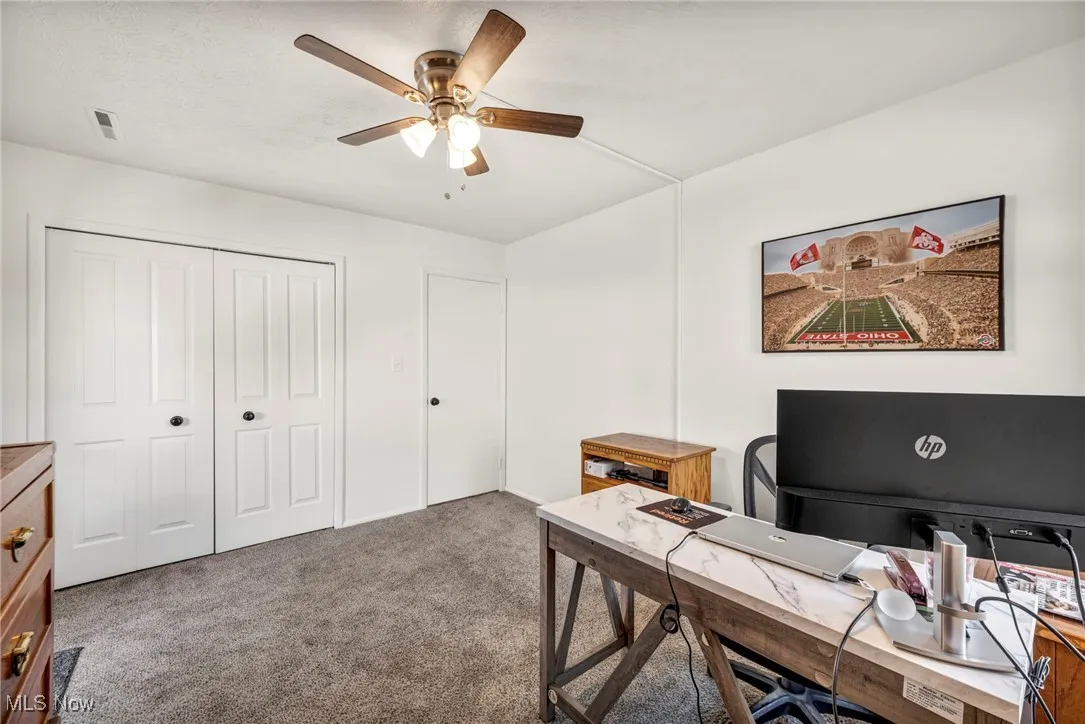 Carpeted home office with a ceiling fan