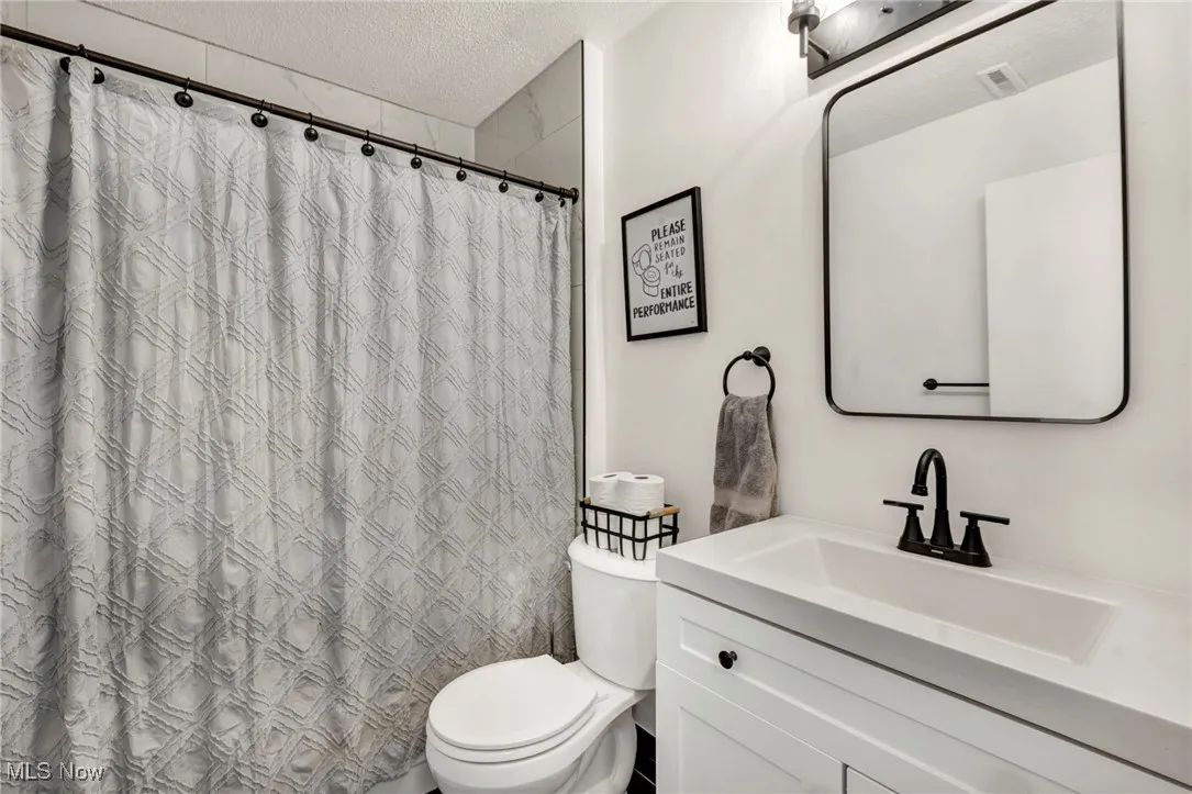 Full bathroom with a textured ceiling, vanity, and a shower with curtain