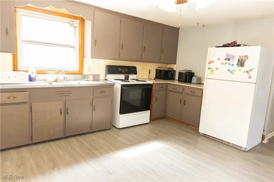 Kitchen with white appliances, light countertops, tasteful backsplash, light wood finished floors, and gray cabinetry