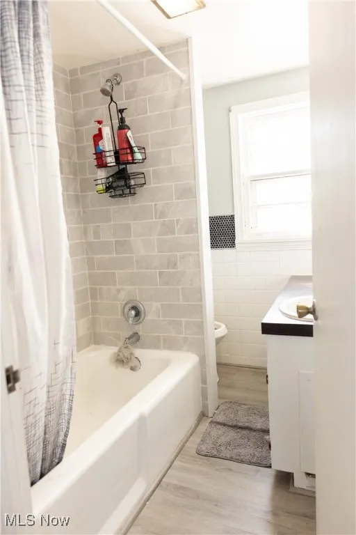 Bathroom with tile walls, shower / bath combo with shower curtain, vanity, light wood-type flooring, and wainscoting