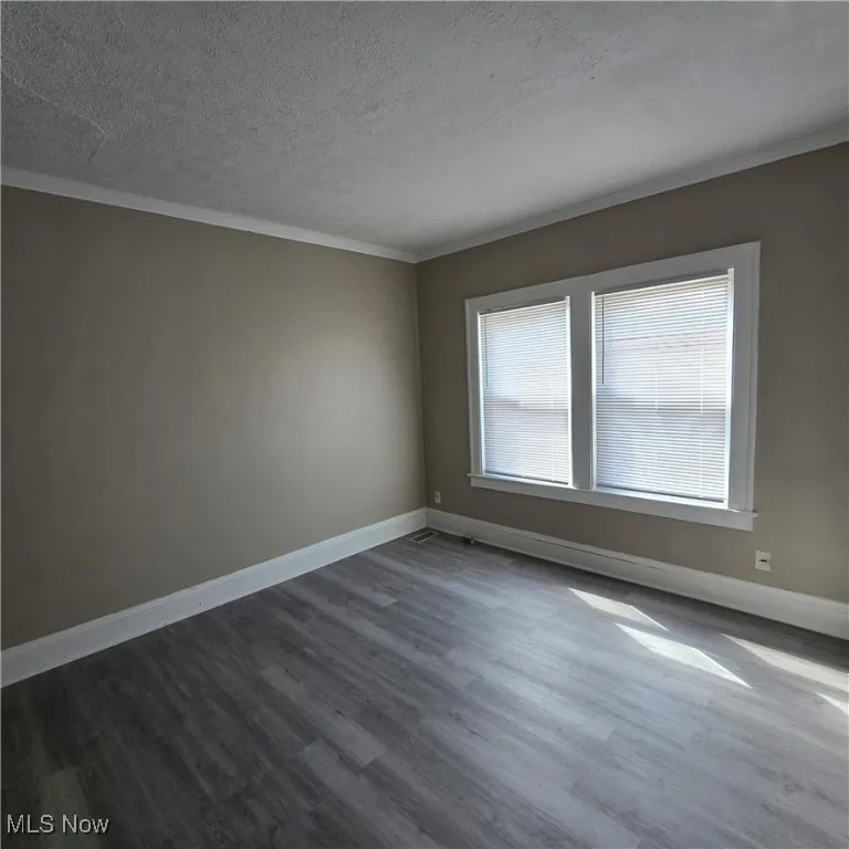 Empty room featuring dark wood-type flooring, a textured ceiling, crown molding, and baseboards