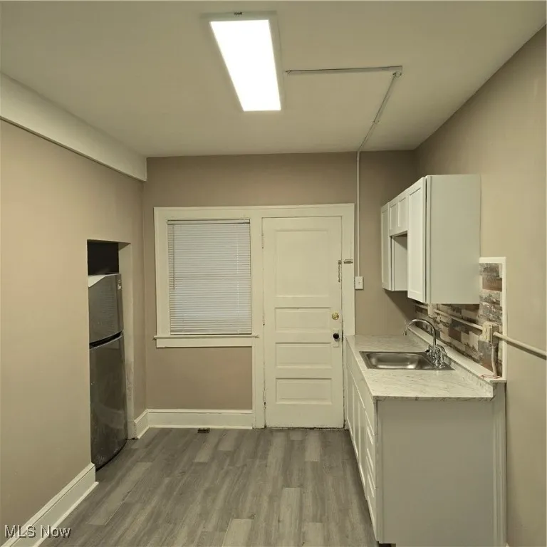 Kitchen with refrigerator, wood finished floors, a sink, light countertops, and white cabinetry