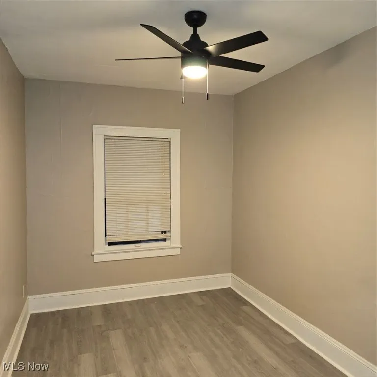 Empty room featuring wood finished floors, baseboards, and ceiling fan