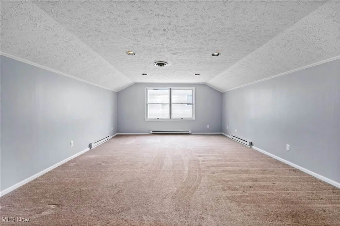 Bonus room with a baseboard heating unit, carpet flooring, vaulted ceiling, and a textured ceiling