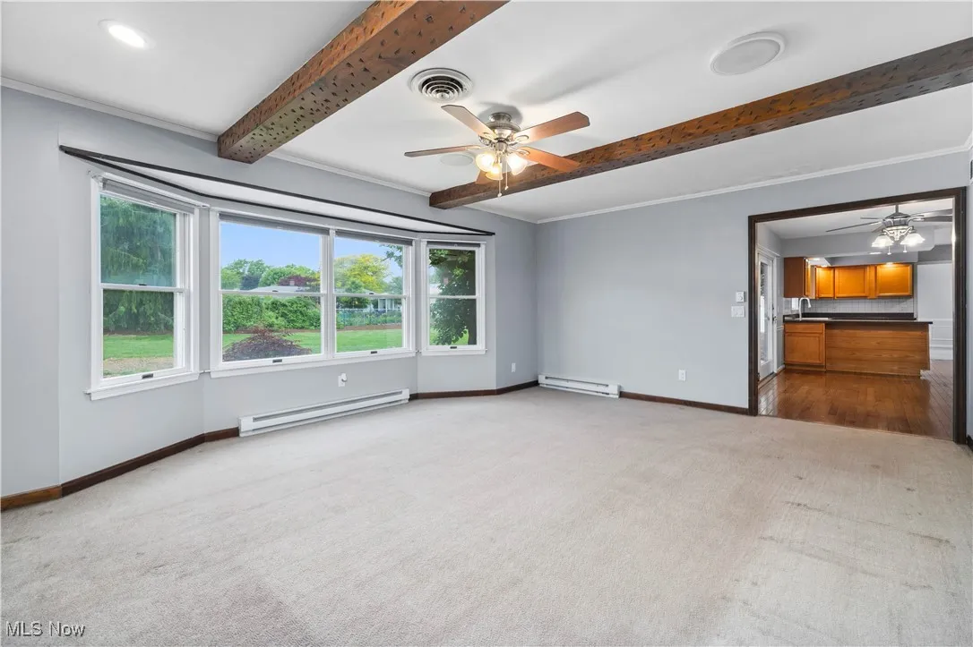 Carpeted spare room featuring a baseboard radiator, ceiling fan, and beam ceiling