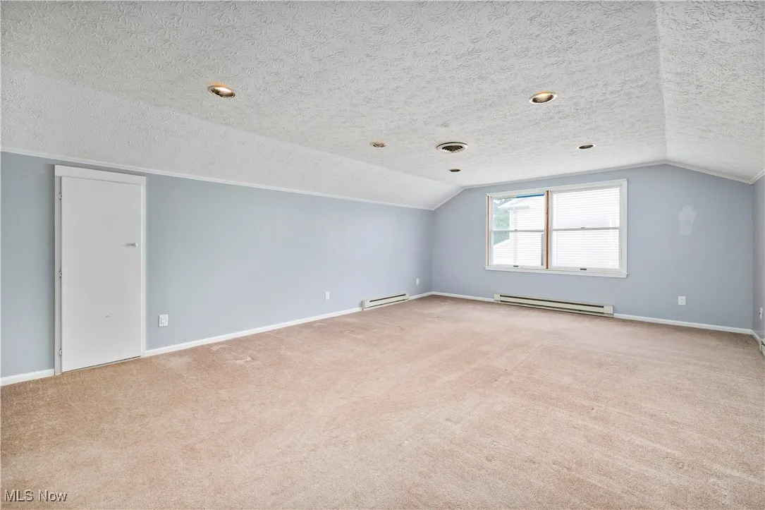 Additional living space featuring a baseboard radiator, light carpet, lofted ceiling, and a textured ceiling
