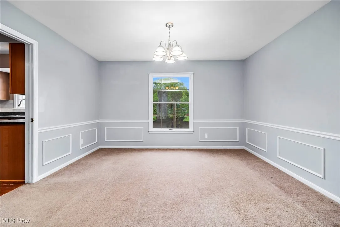 Carpeted empty room featuring a chandelier, a wainscoted wall, and a decorative wall