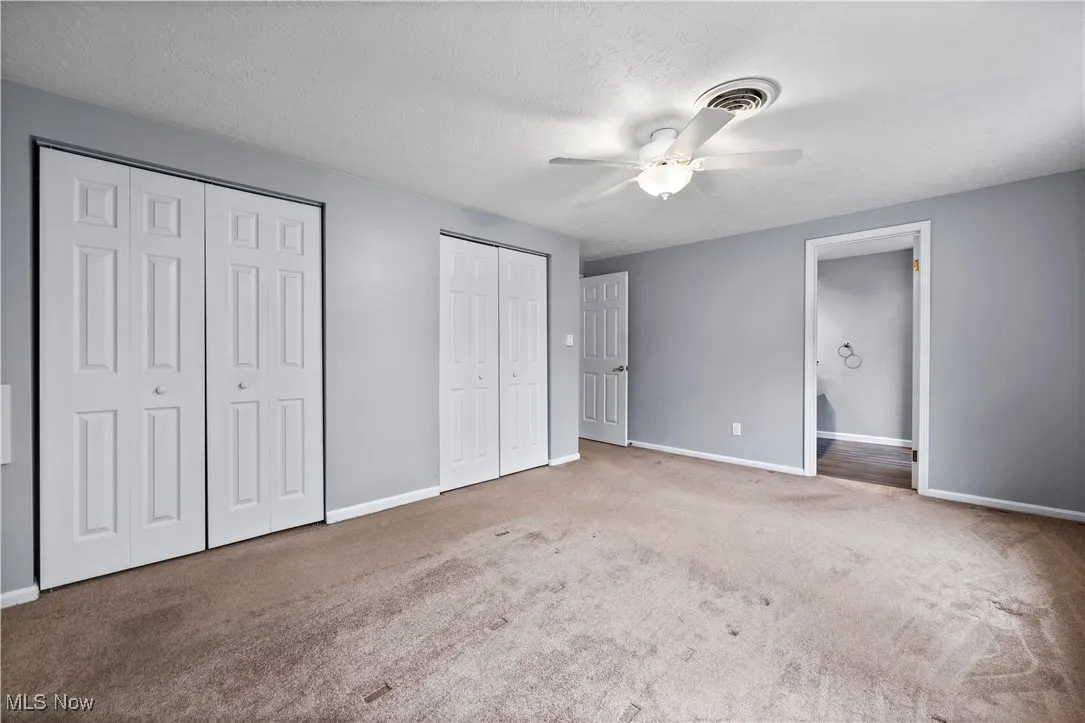 Unfurnished bedroom with multiple closets, carpet floors, ceiling fan, and a textured ceiling