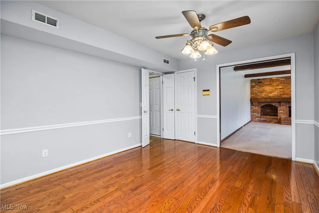 Unfurnished bedroom featuring a fireplace, wood finished floors, and a ceiling fan